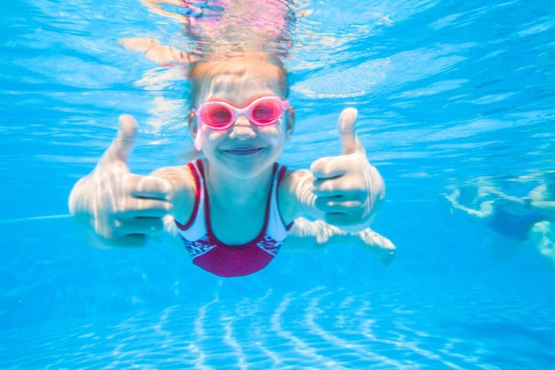 Little girl deftly swim underwater in pool.