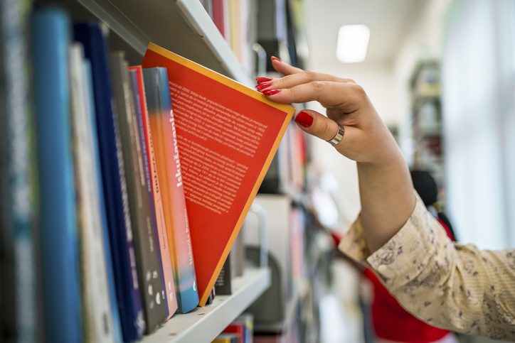 Woman's hand picking a book from a bookstore shelf