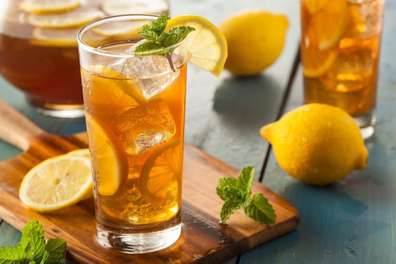 A glass of iced tea and lemons on a cutting board.