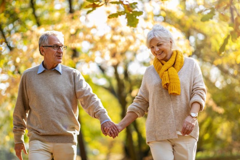 older couple smiles and holds hands while walking