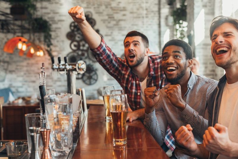 A group of guys watching sports at a modern looking bar.
