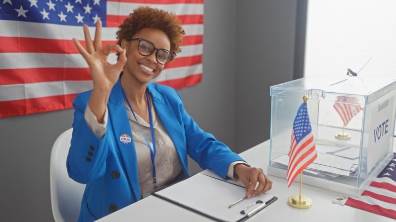 Woman sits at voting table smiling at camera.