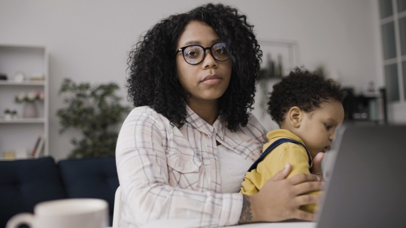 Photo of exhausted woman holding her child, looking at the camera.