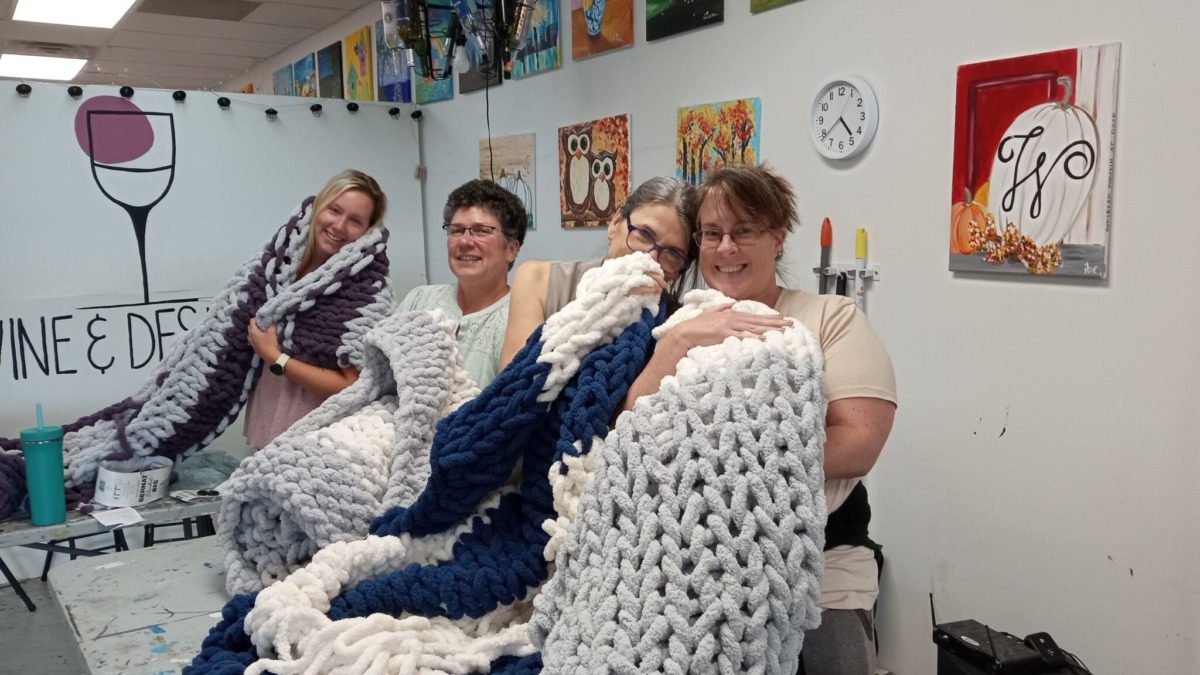 Women showing off blankets they made at camp. 