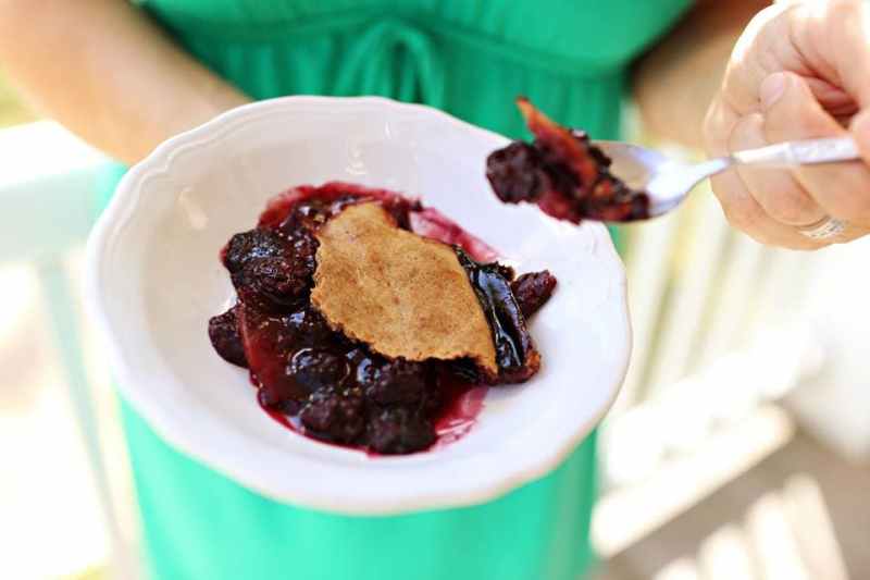 white hands hold a white bowl of blackberry sonker