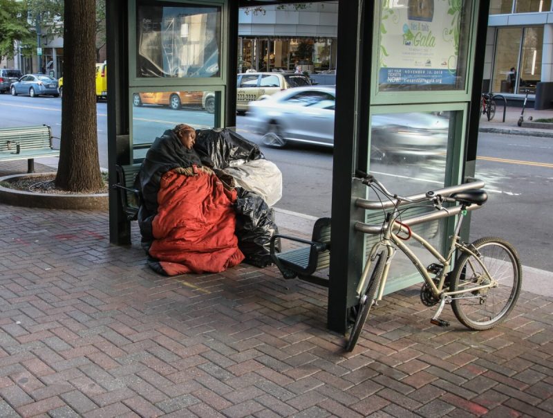 Photo of a homeless woman, with bags of possessions, sleeps at a bus stop in NC.