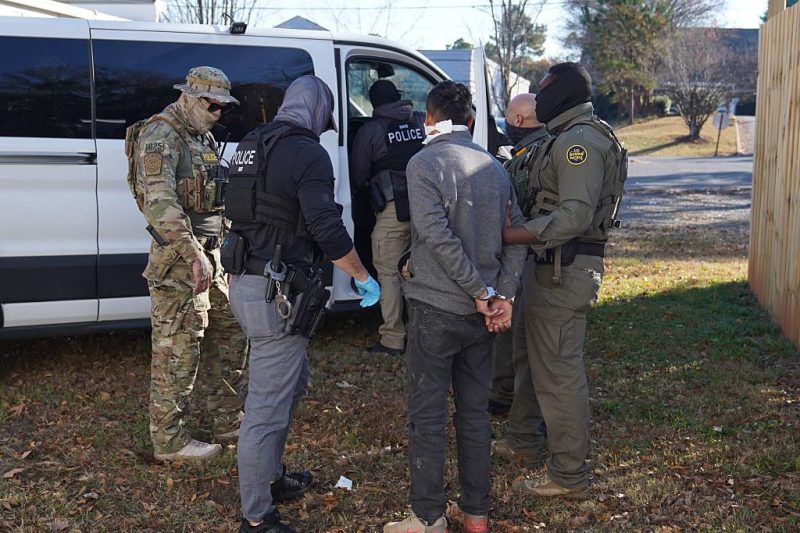 Photo of federal immigration agents blindfolding and arresting a man.