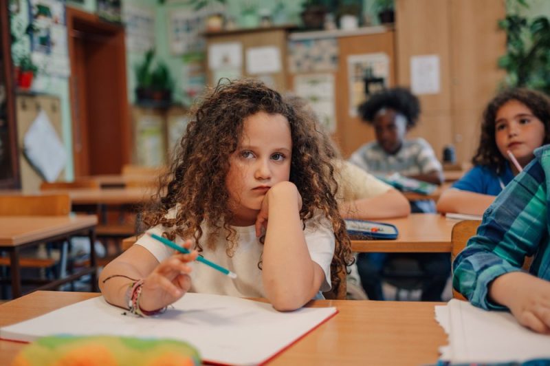Photo of a young girl looking upset at her desk in the middle of class.